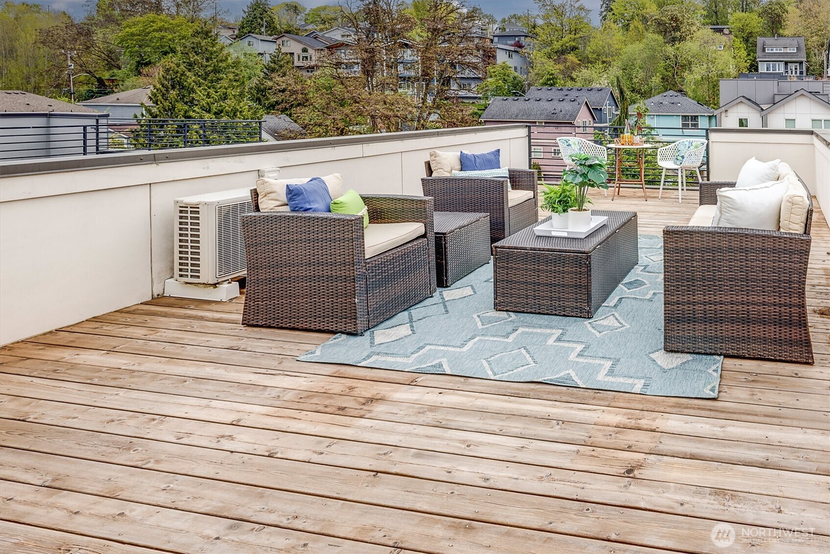 Rooftop deck with wicker seating, a patterned rug, and a dining area overlooking neighboring homes.