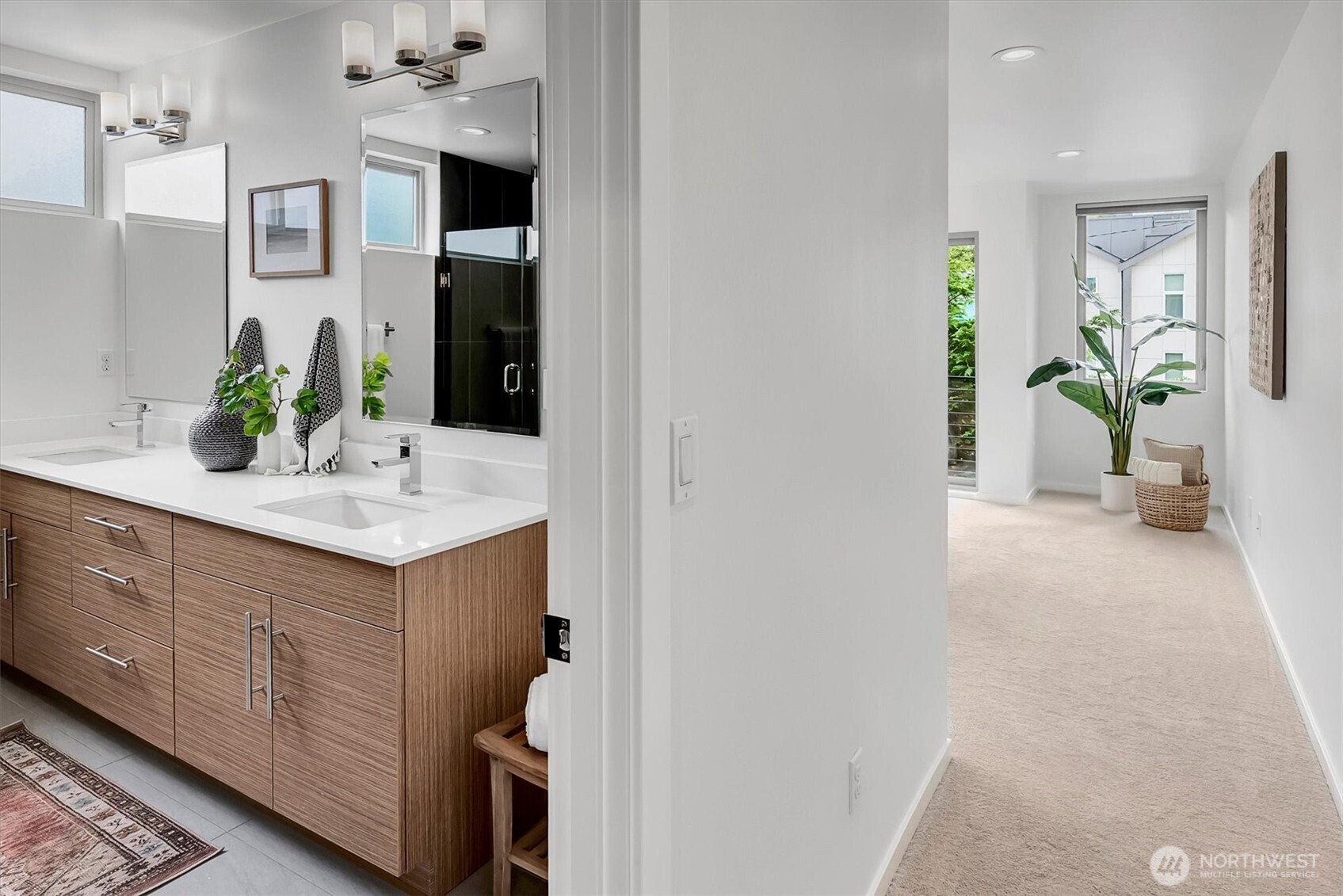 Bathroom with a double-sink wood vanity beside a carpeted hallway and window.