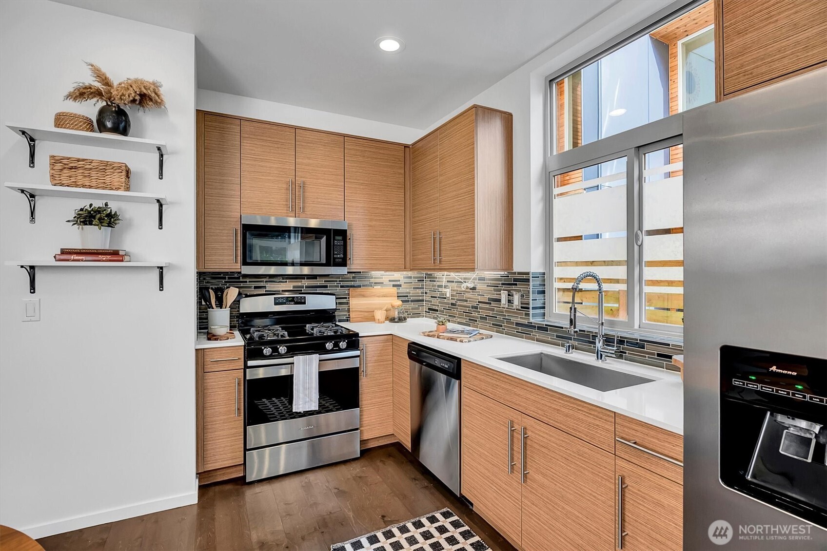 Modern kitchen with warm wood cabinets, stainless steel appliances, and a large window over the sink.