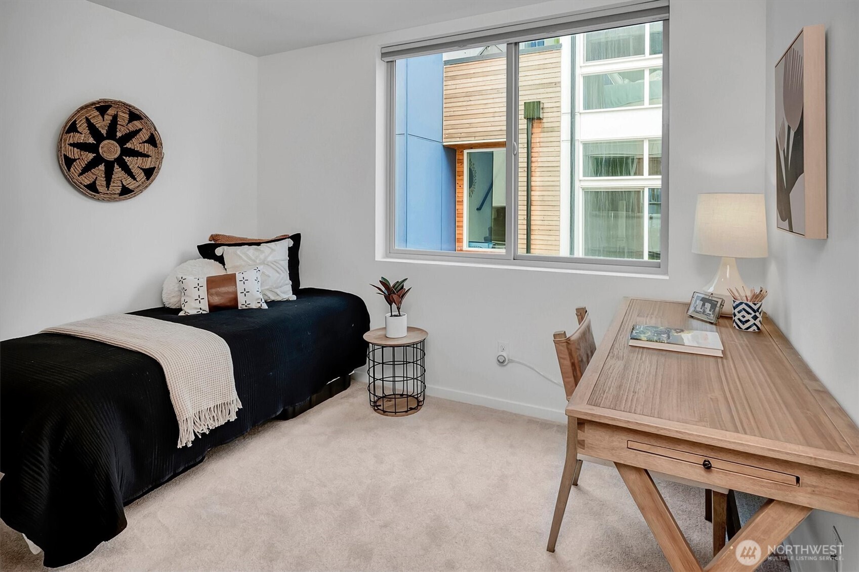 Staged bedroom with a black-covered bed, wooden desk, and large window.