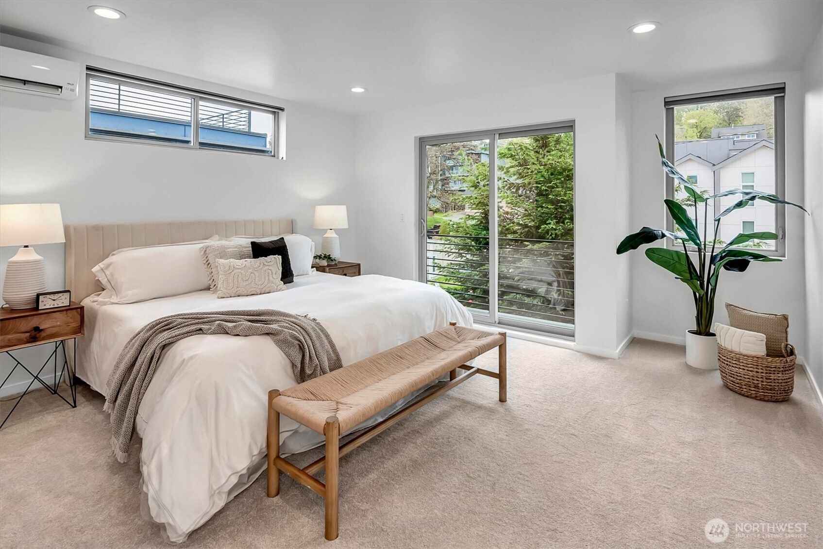 Staged bedroom with a king-size bed, sliding glass doors, and a potted plant beside the window.