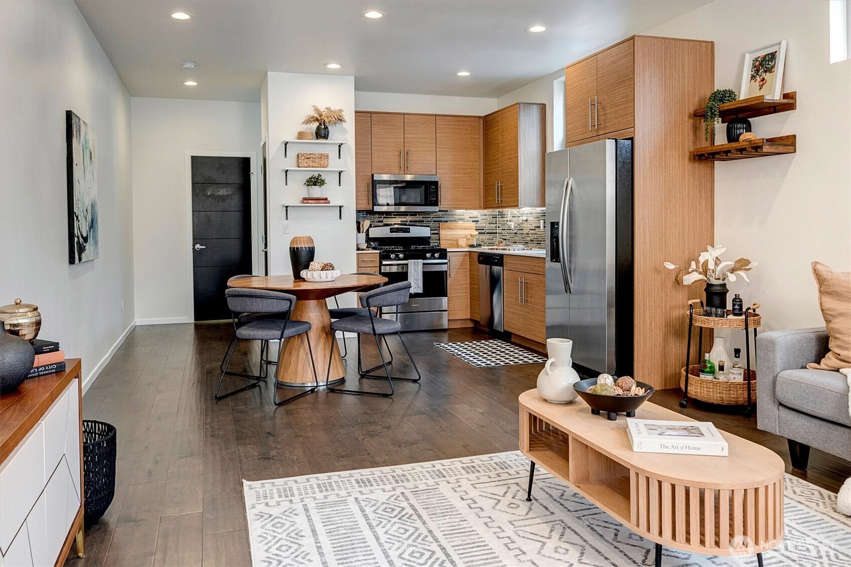 Open-plan kitchen with warm wood cabinets, stainless appliances, and a round dining table.
