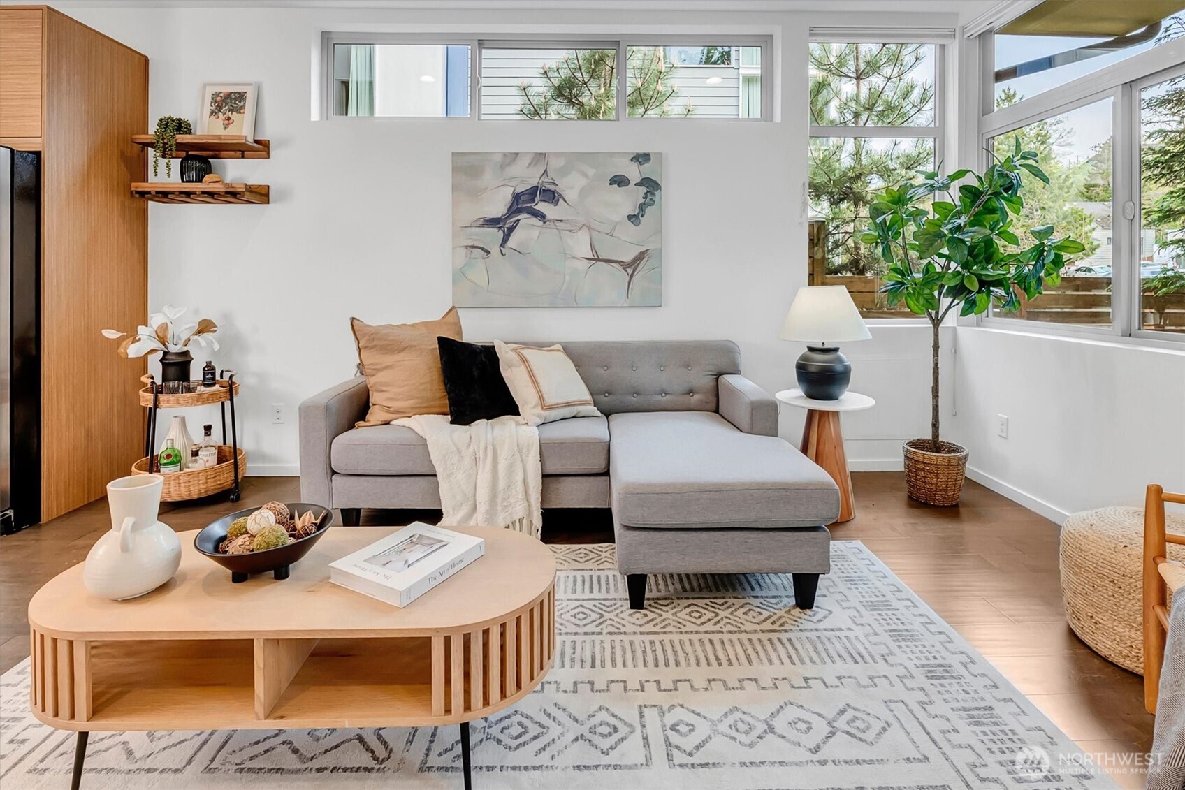 Staged living room with a gray sectional, round wood coffee table, and large windows.