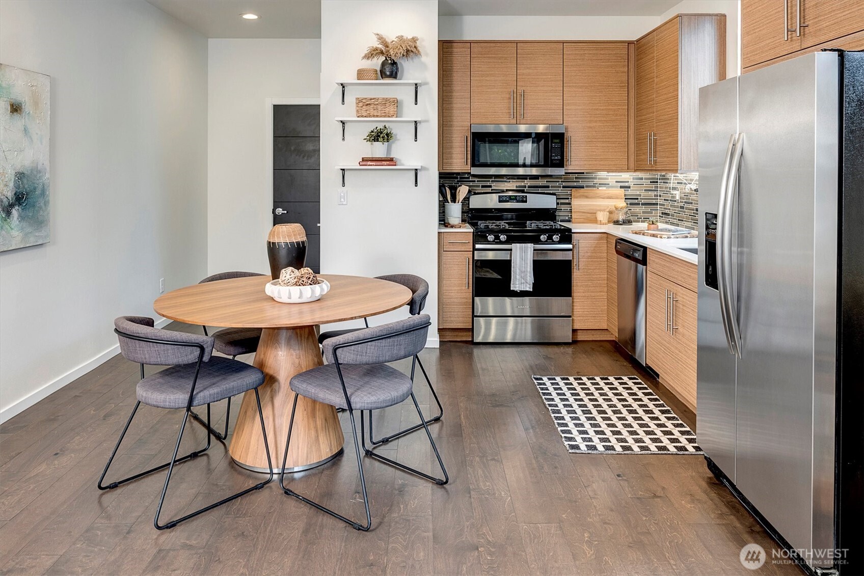 Staged kitchen with wood cabinets and stainless appliances beside a round dining table and four chairs.