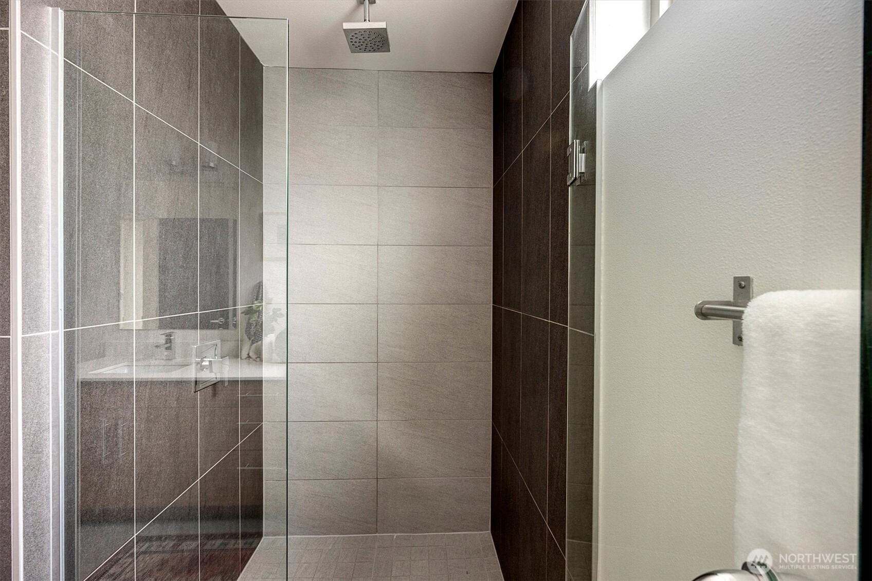 Bathroom with a glass-enclosed shower, large gray tiles, and a square rainfall showerhead.