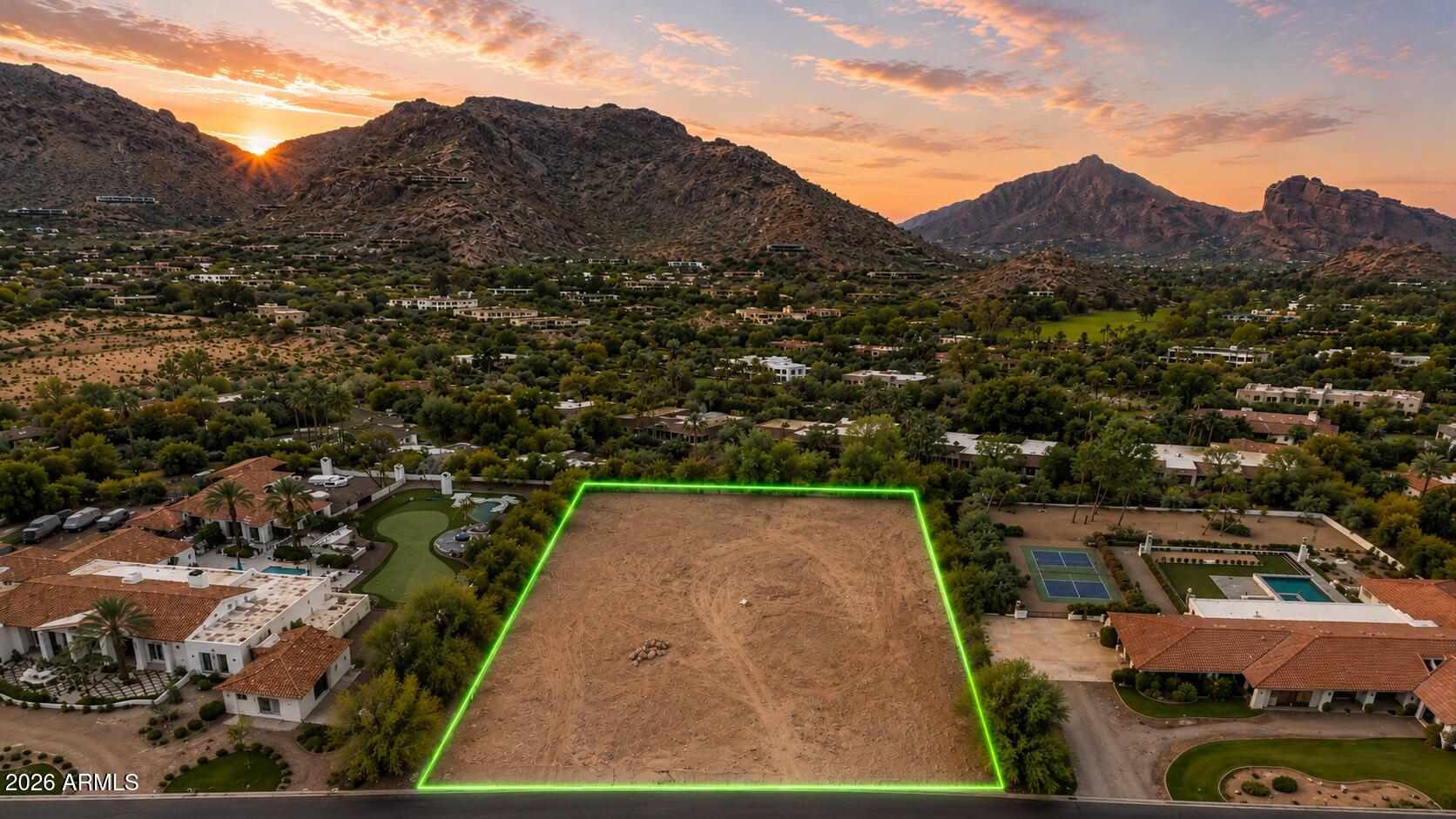 Aerial view of a vacant lot outlined in green, with Scottsdale homes and mountains at sunset.