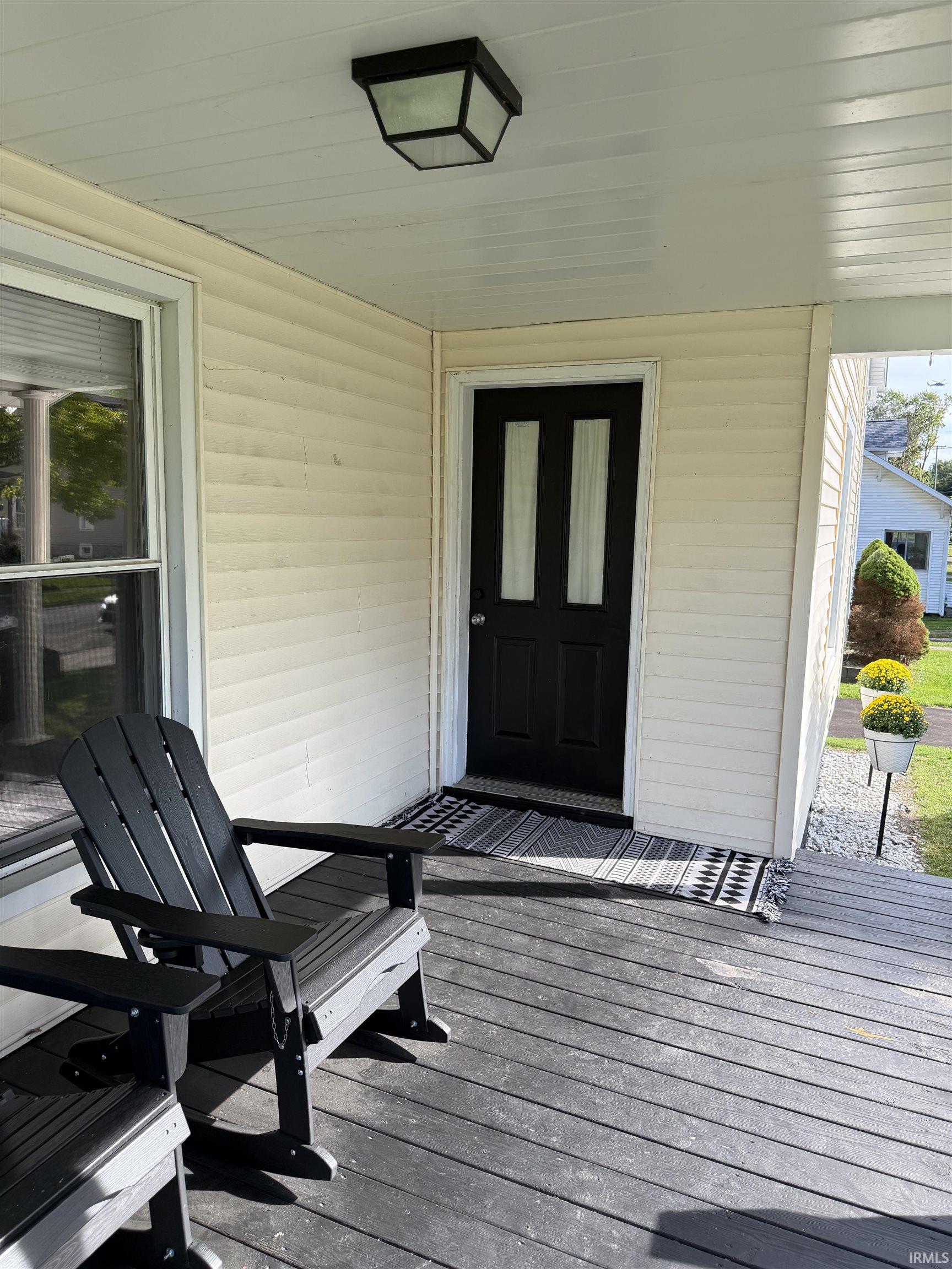 Covered front porch with black entry door, Adirondack chairs, and patterned doormat.