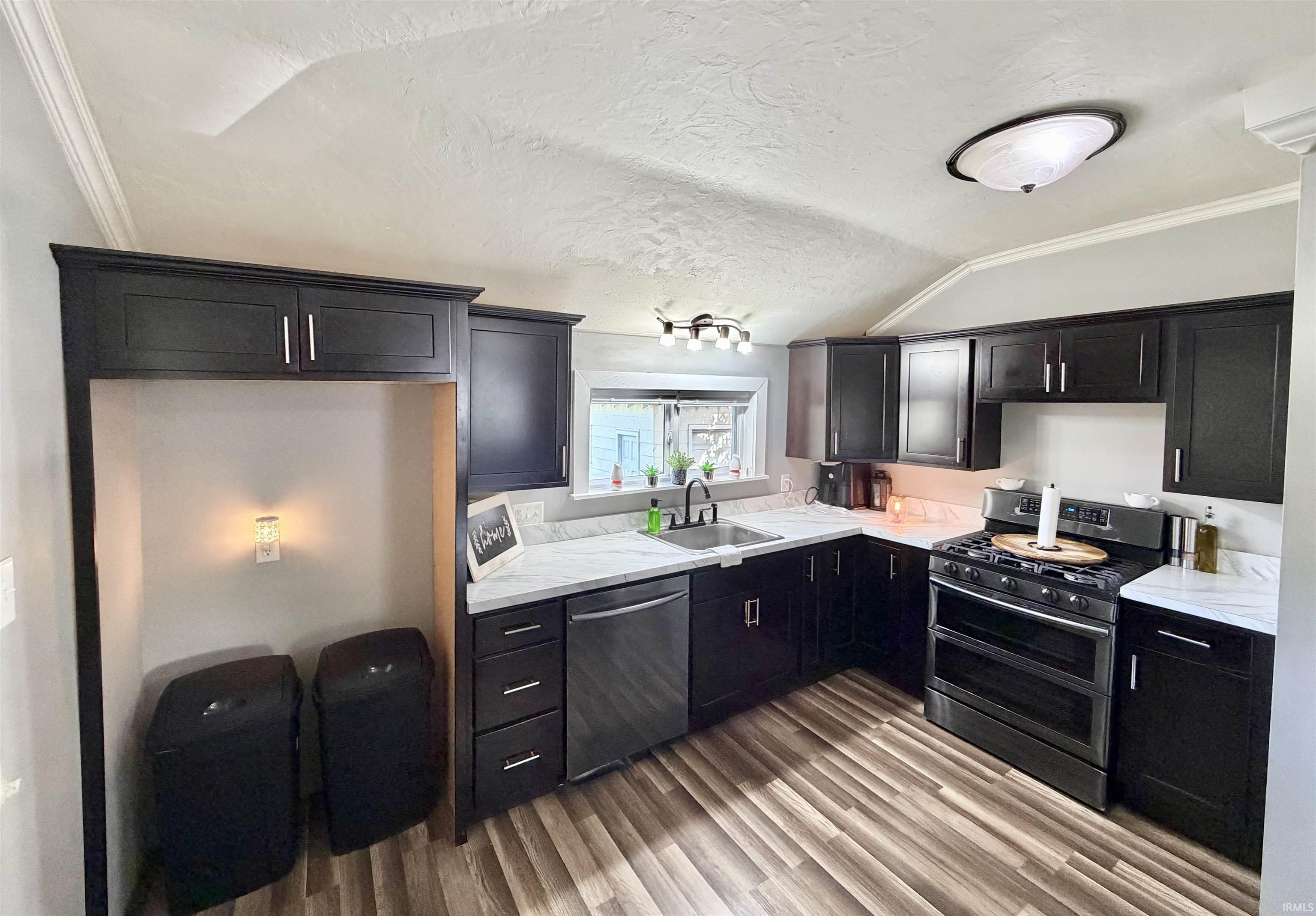 Kitchen with dark cabinets, marble-pattern counters, stainless steel appliances, and wood-look flooring.