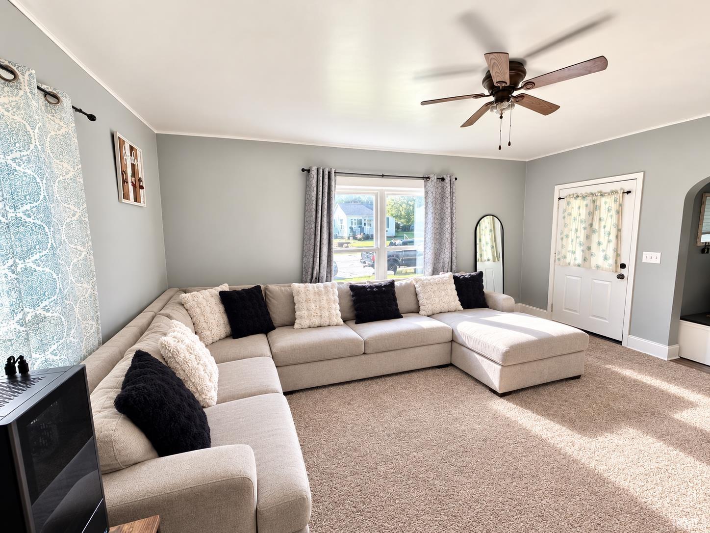 Living room with a large cream sectional, patterned curtains, and a wood-toned ceiling fan.