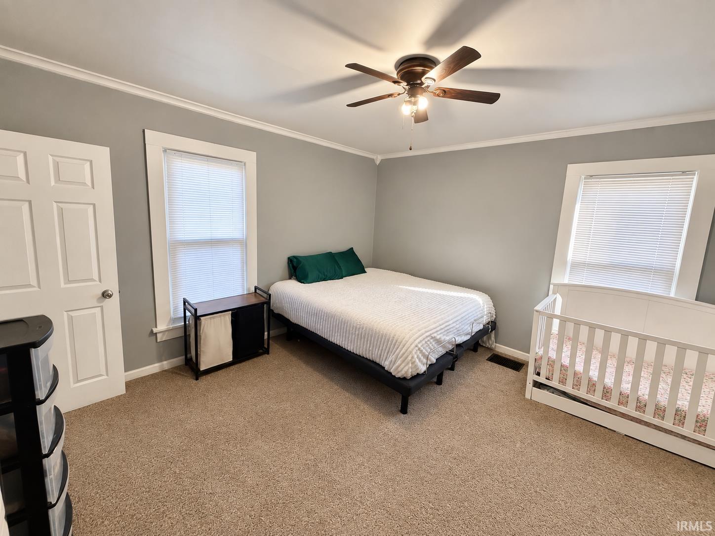 Bedroom with a white-bedded bed and white crib, gray walls, and beige carpet.