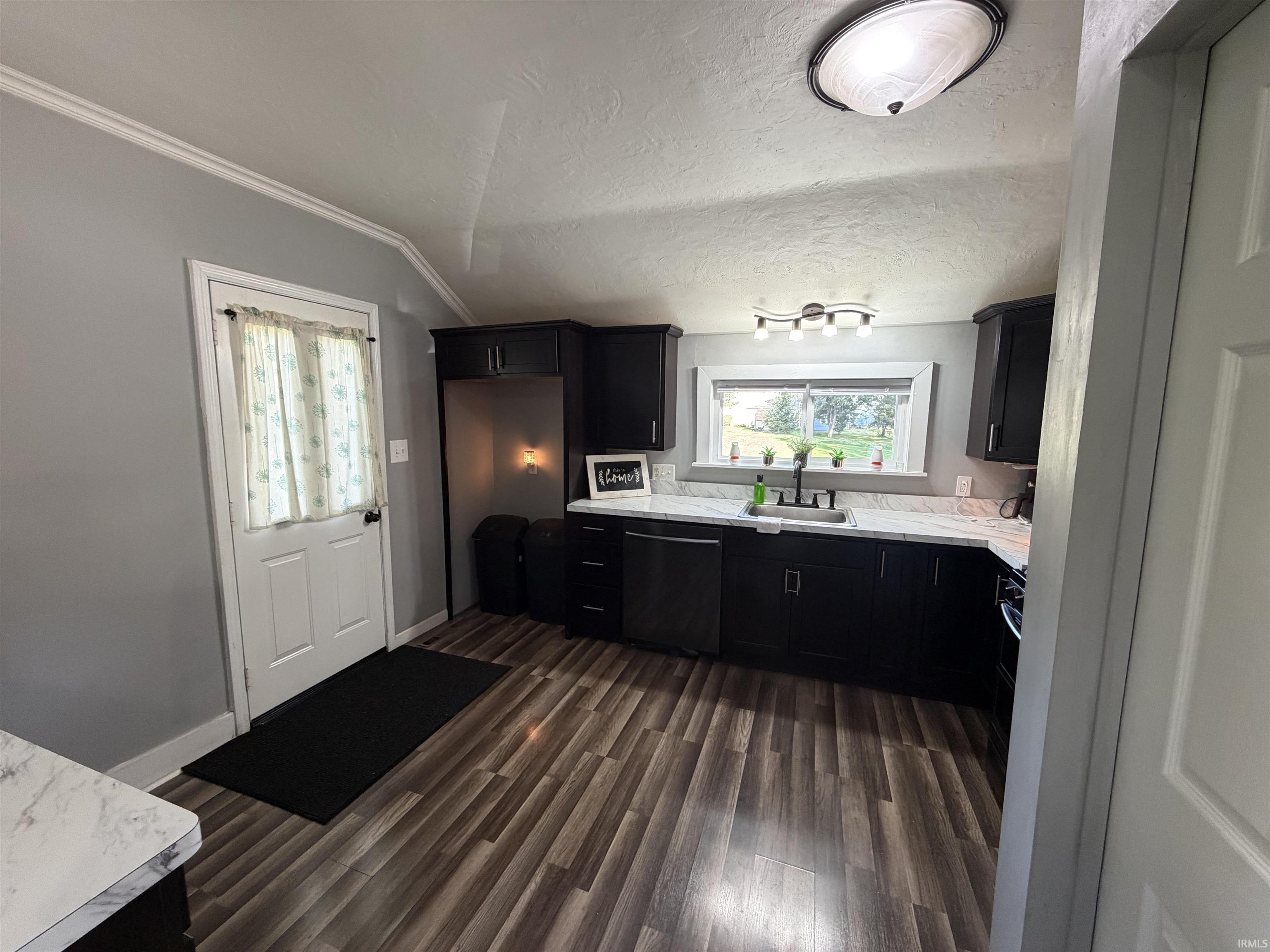Kitchen with dark cabinets, a marble-look countertop, and a sink beneath a wide window.