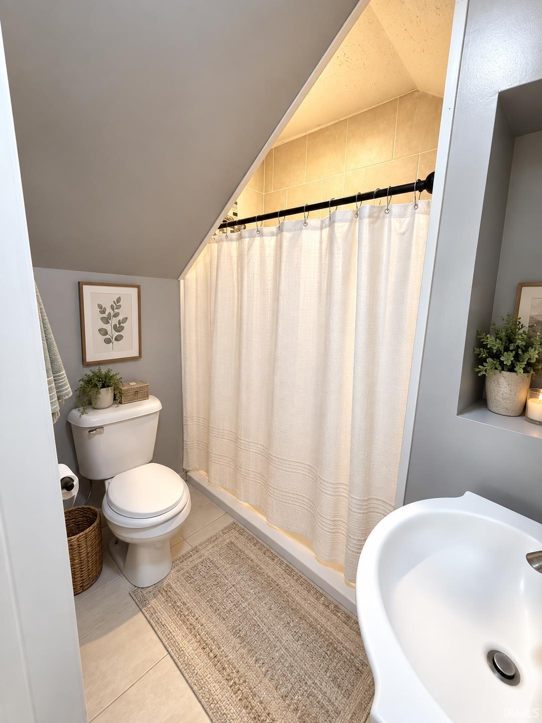 Bathroom with a sloped ceiling, curtained tiled shower, toilet, and partial view of a bathtub.