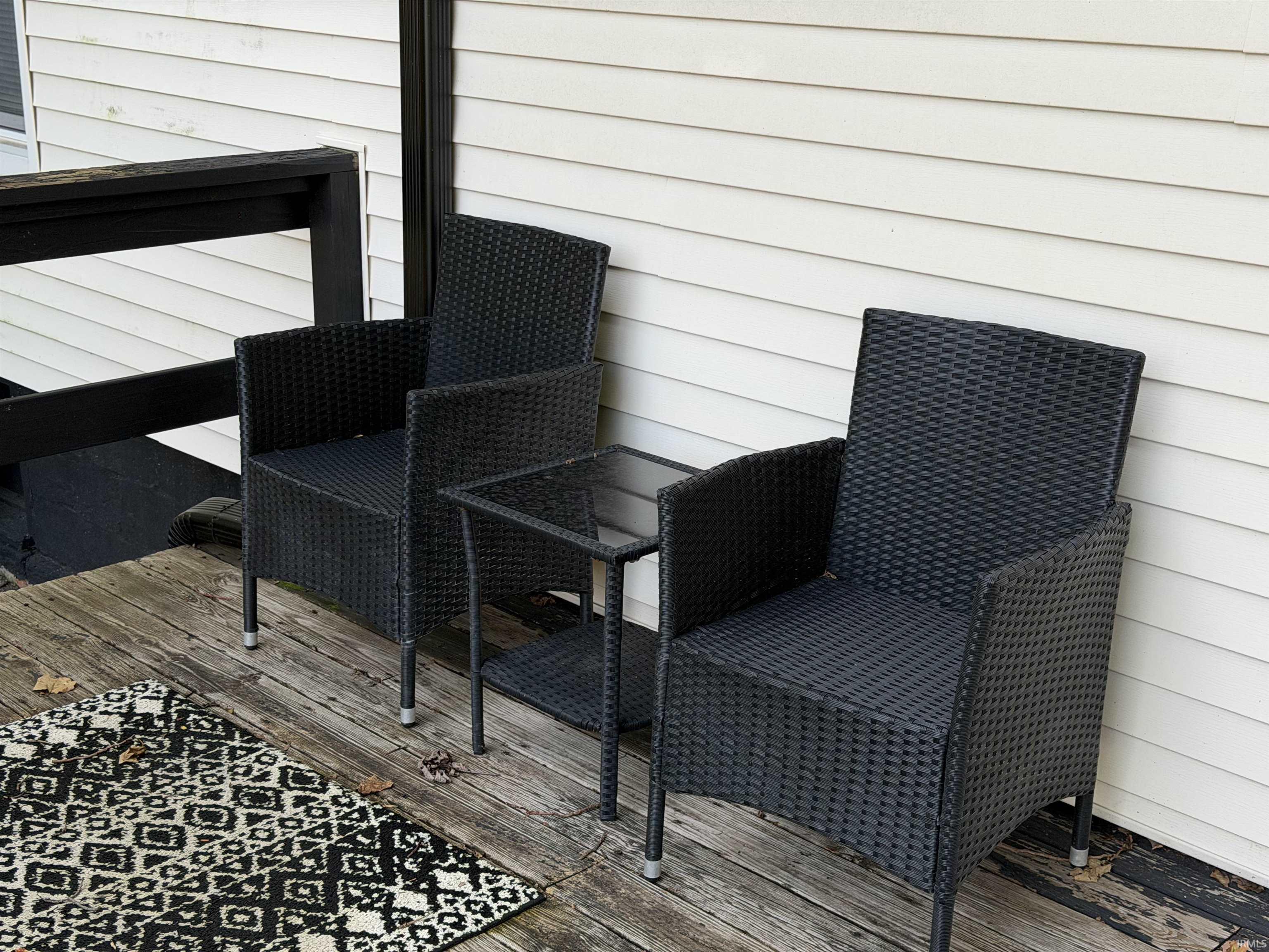 Deck seating with two black woven chairs, a glass-top table, and a patterned rug.