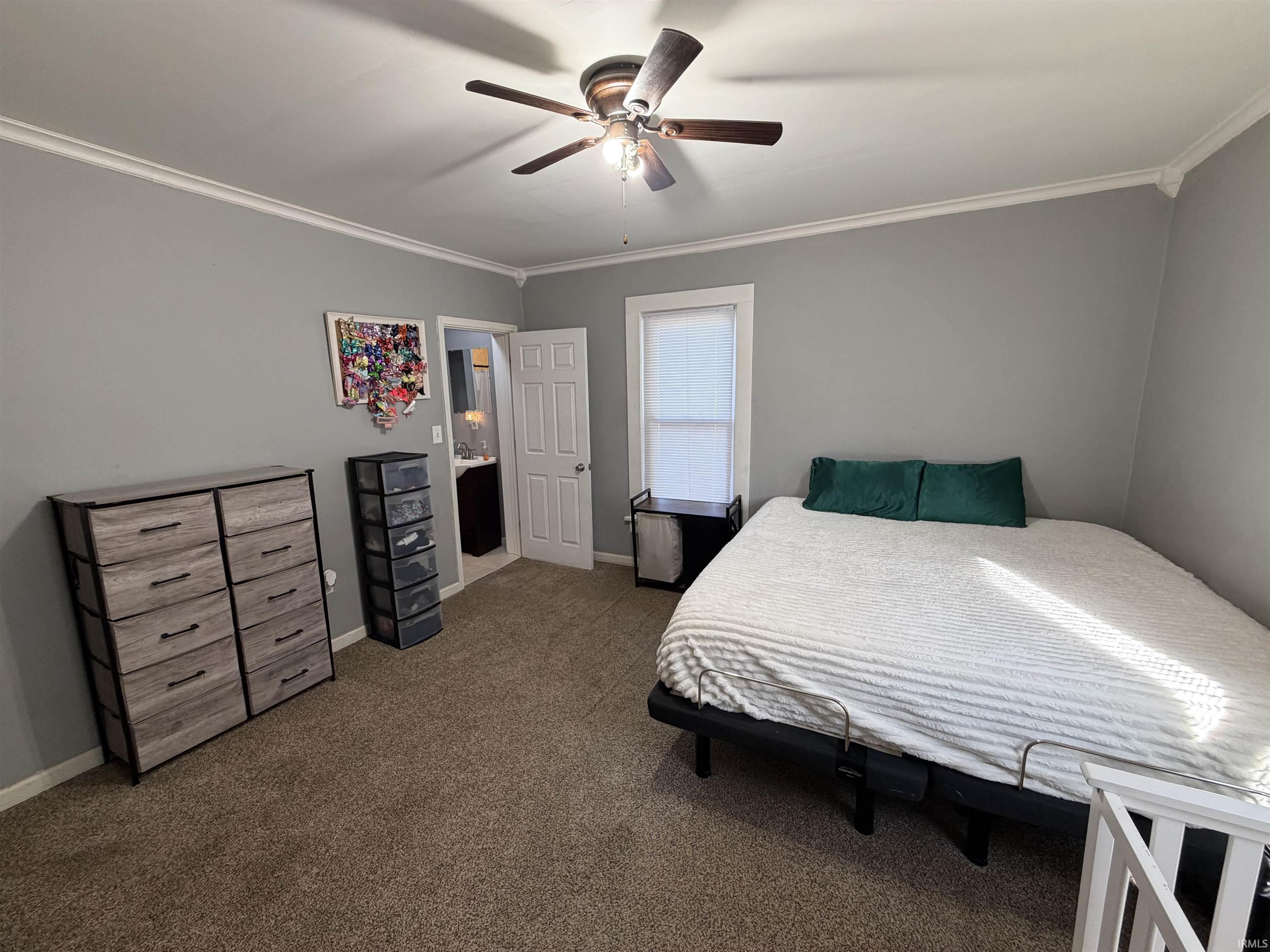 Bedroom with a white bed and green pillows, gray walls, brown carpet, and an open door to the bathroom.