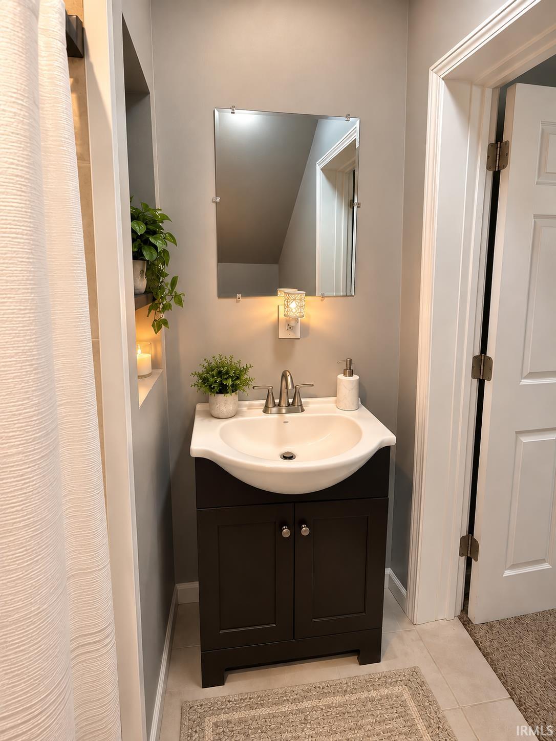 Bathroom vanity with a white sink, dark cabinet, wall mirror, and decorative plants.