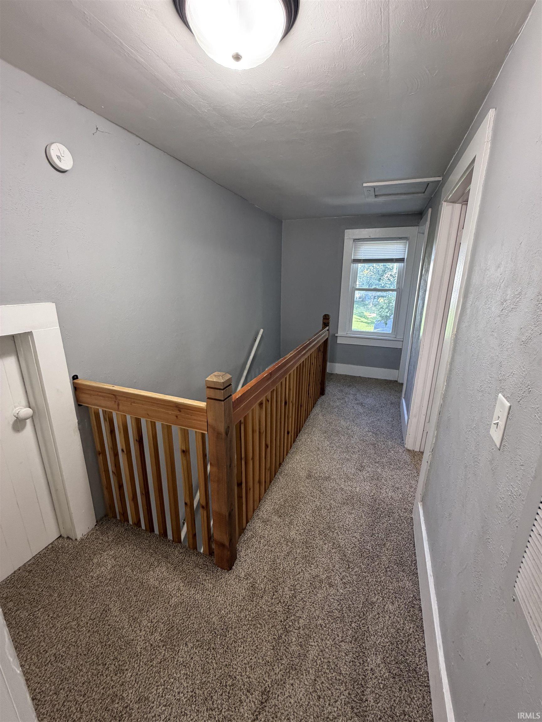 Upstairs landing with carpet, a wooden stair railing, and a window at the end of the hall.