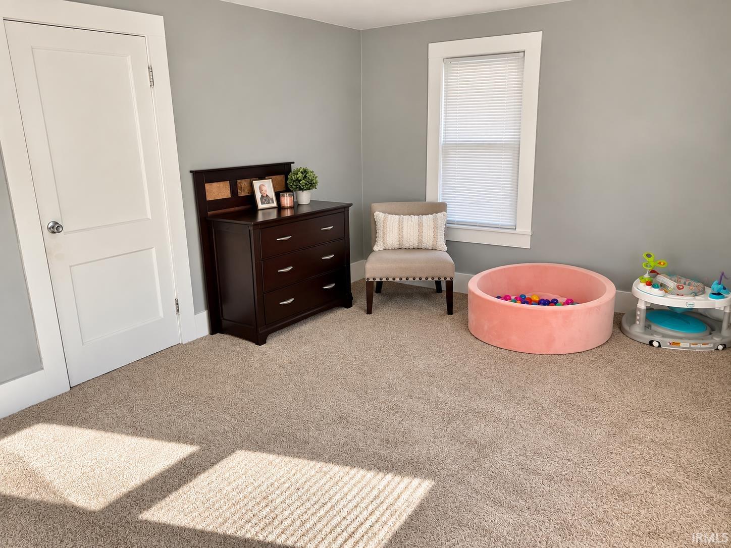 Nursery with a dark wood dresser, upholstered chair, pink ball pit, and baby activity center.