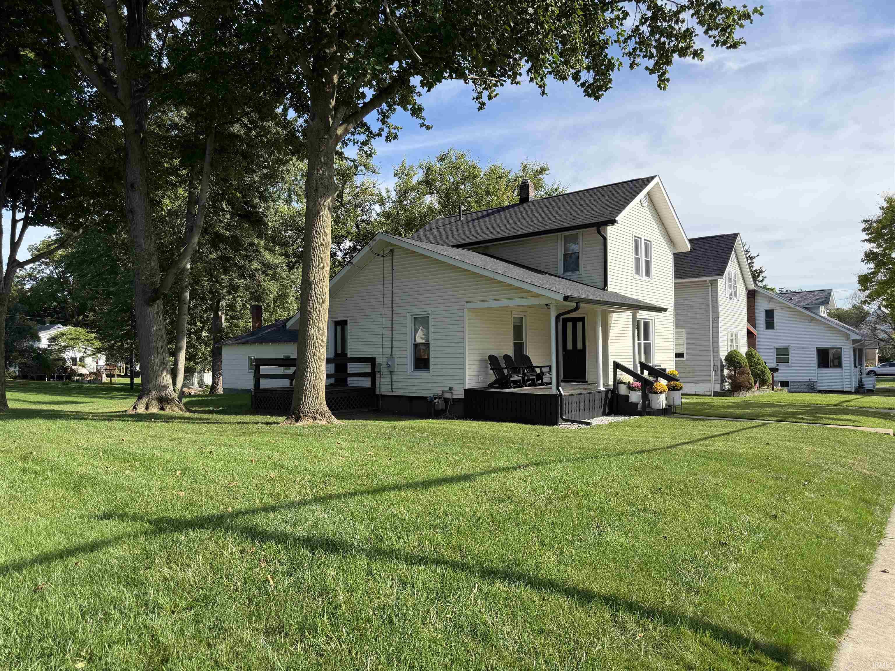 Two-story house with a covered porch, mature shade trees, and a broad green lawn.