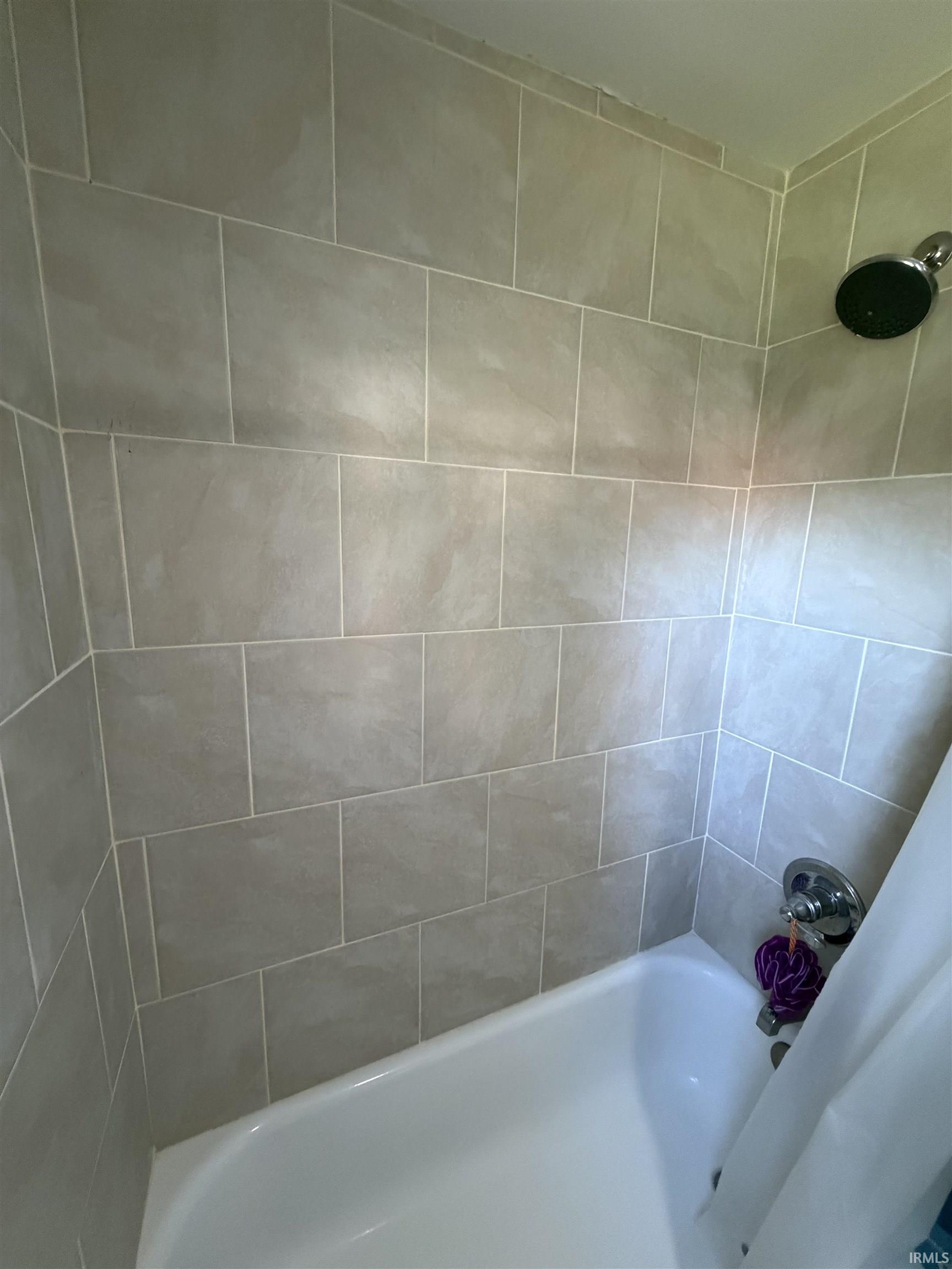 Bathroom tub and shower with large neutral tile and a dark round showerhead.