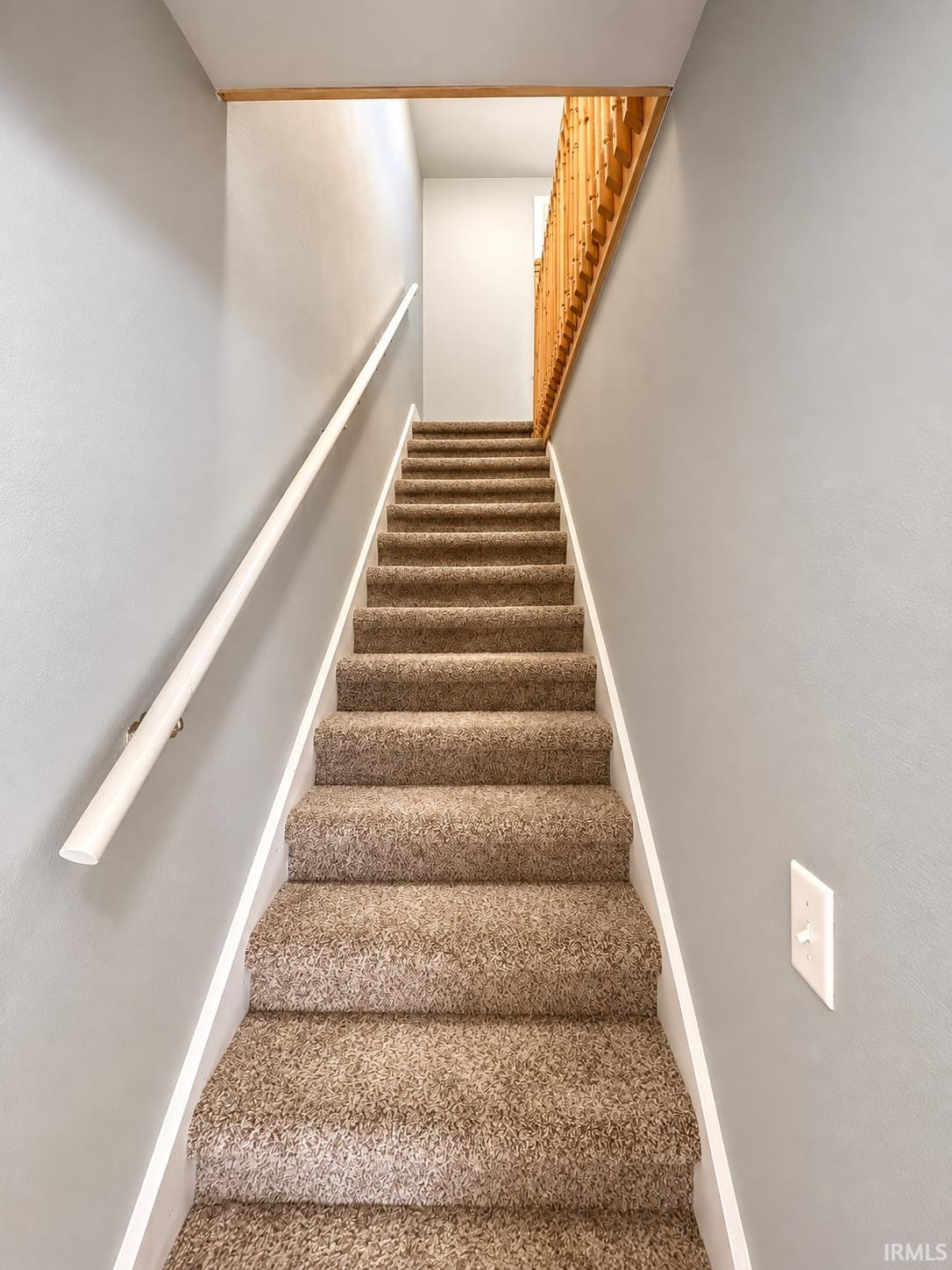 Carpeted staircase with a white handrail and wooden railing.