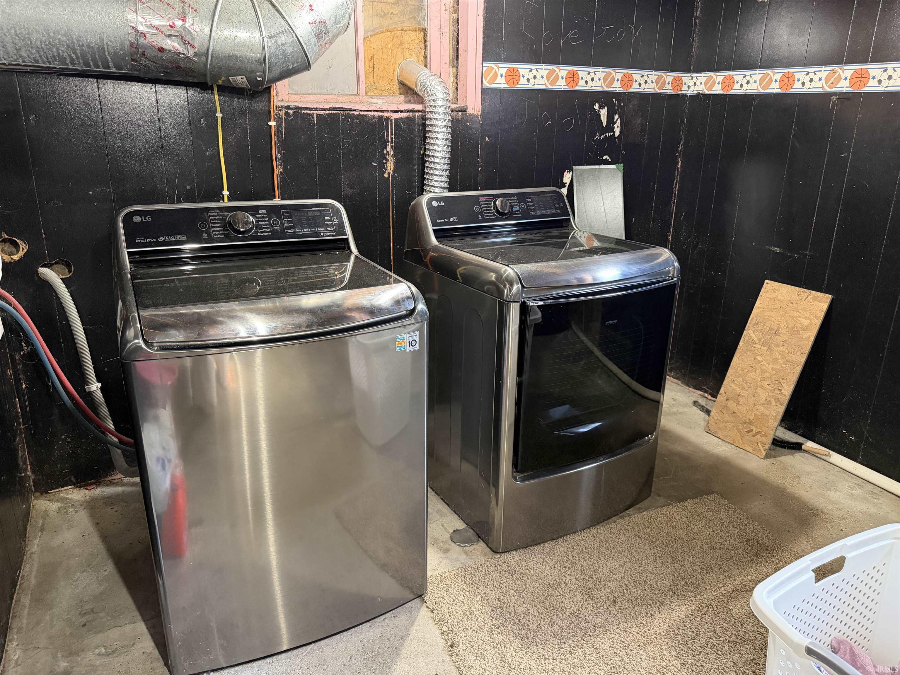 Basement laundry area with two stainless steel LG top-loading machines and exposed ductwork.