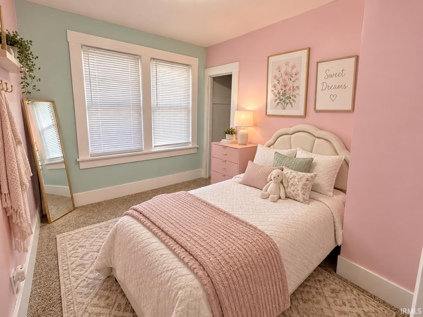 Bedroom with a white bed, pink and sage-green walls, and framed floral artwork.