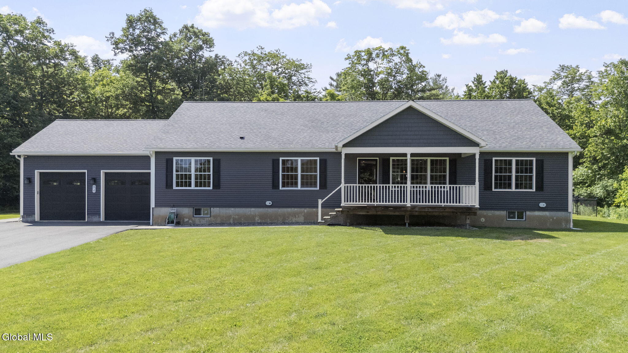 Single-story gray home with two-car garage, covered porch, and broad green lawn.