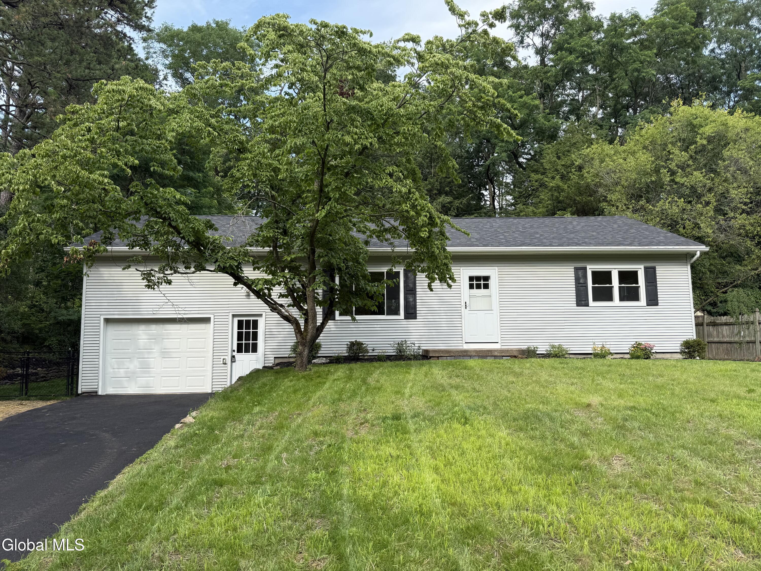 Single-story white house with an attached garage, partly shaded by a large leafy tree.