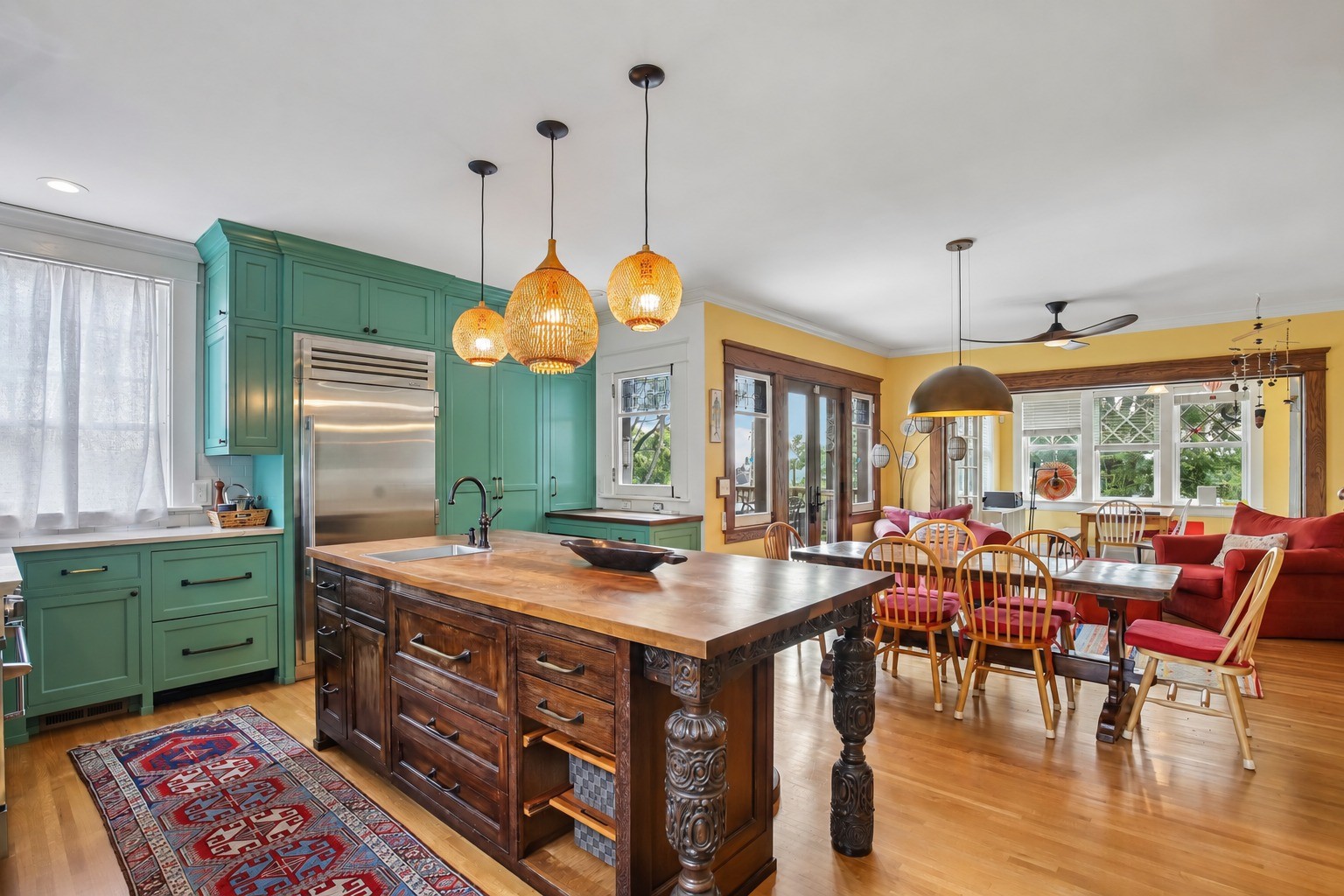 Kitchen with teal cabinetry, a carved wood island, woven pendant lights, and an adjoining dining area.