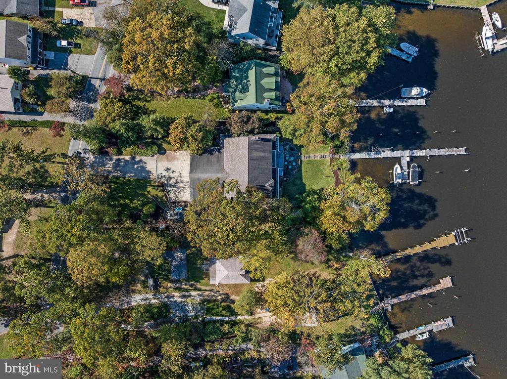 Waterfront home with a tree-lined yard, long dock, and boats on the water.