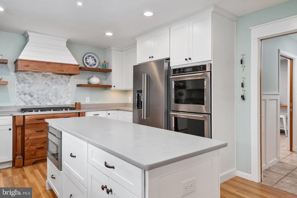 Kitchen with a large white island, stainless steel appliances, and a wood-accented range hood.
