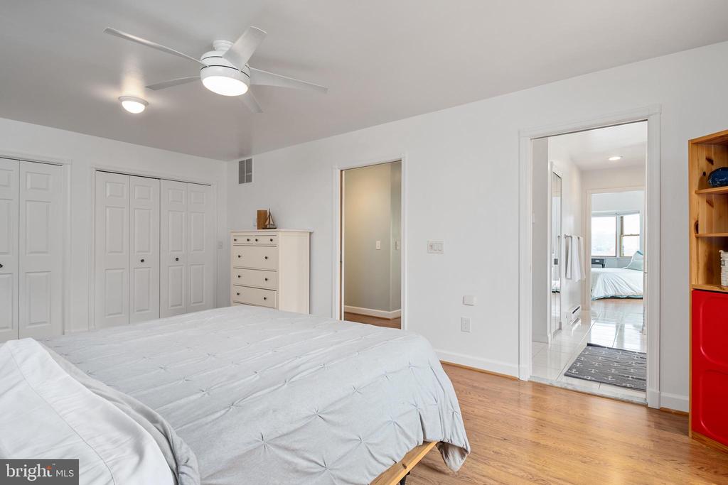 Bedroom with white bedding, multiple closets, a ceiling fan, and hardwood flooring.