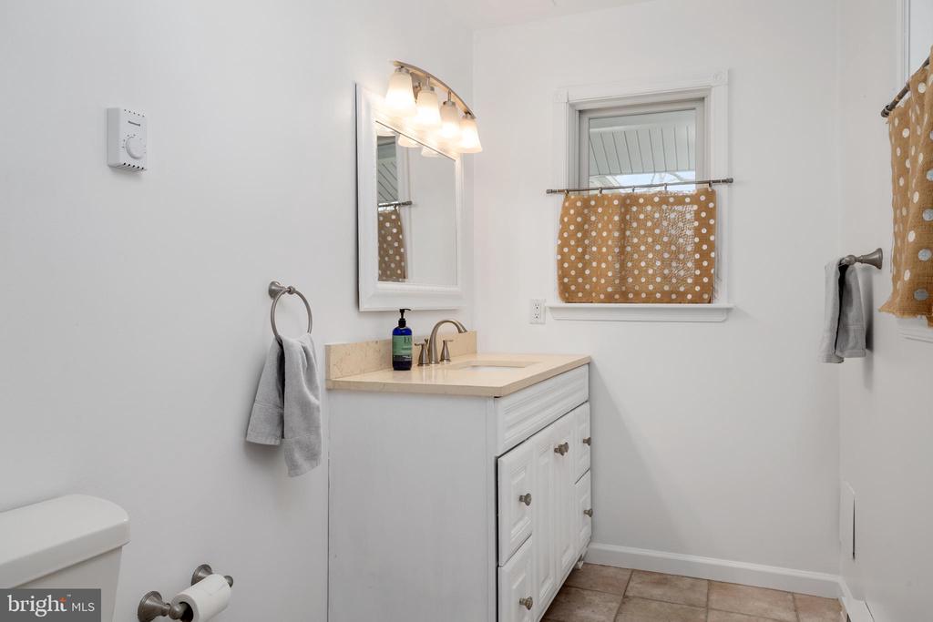 Bathroom with a white vanity and beige countertop beneath a mirror, beside a window with a tan polka-dot curtain.
