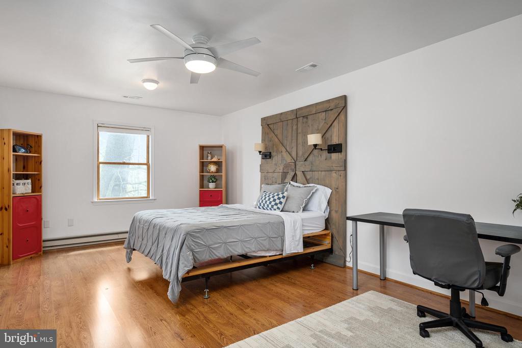 Bedroom with a rustic wood headboard, hardwood floors, and a desk beside the bed.