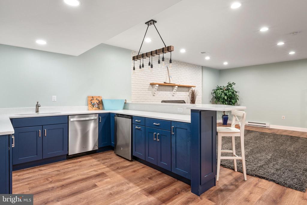 Kitchen with navy cabinets, stainless appliances, white brick backsplash, and a breakfast bar.