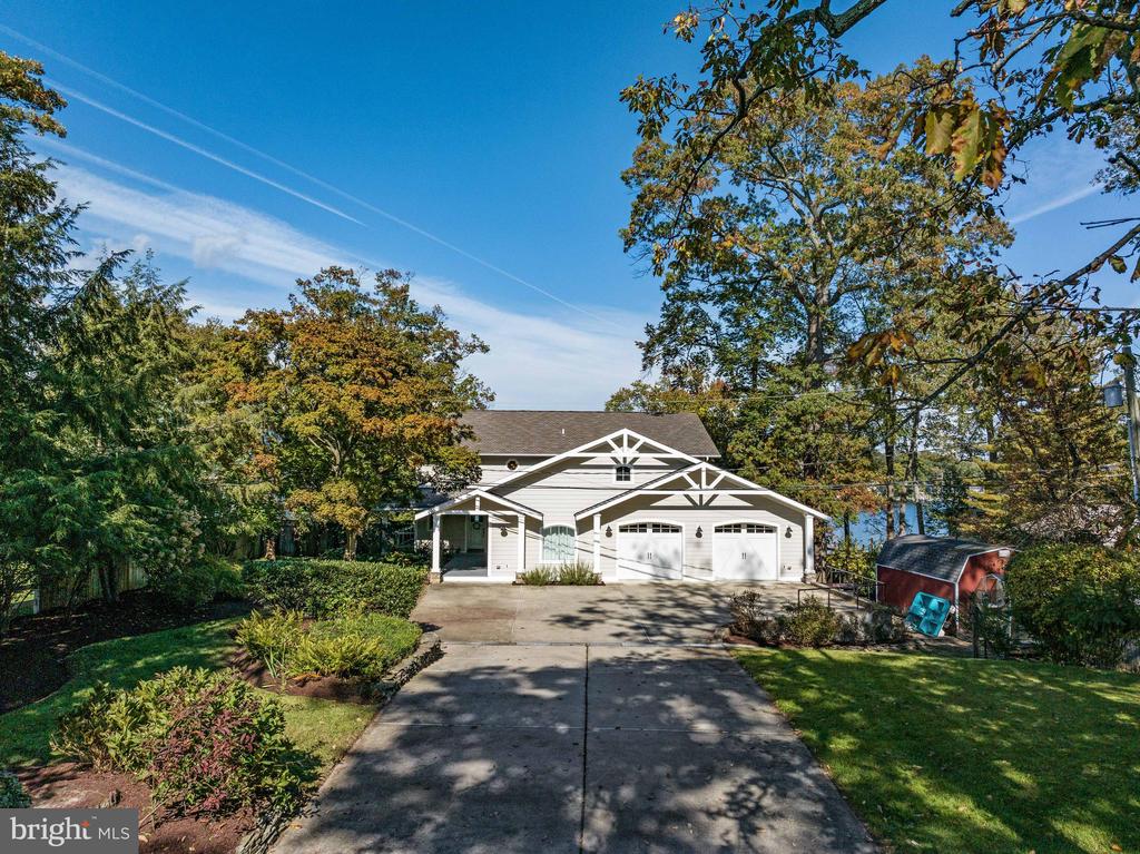 White house with timber-trimmed gables, a two-car garage, and a tree-lined driveway.