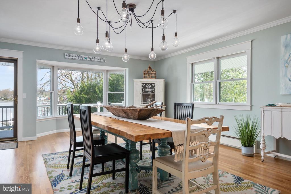 Dining room with a rustic wood table, eclectic chairs, and large windows overlooking the water.