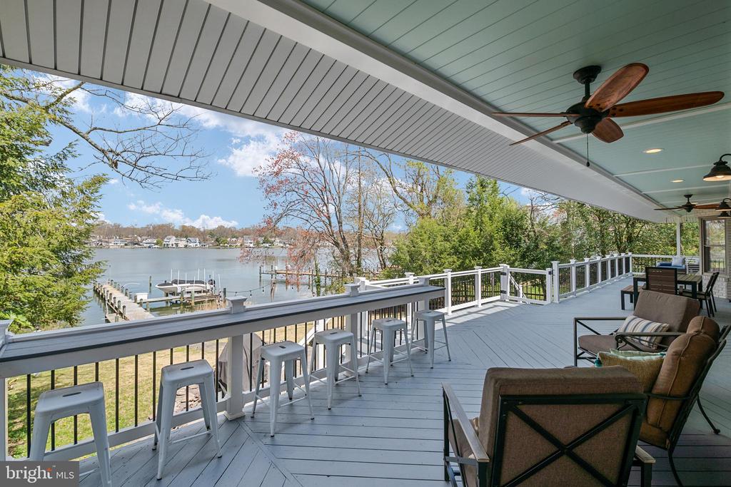 Covered deck overlooking the water, with bar stools, a ceiling fan, and a dock below.