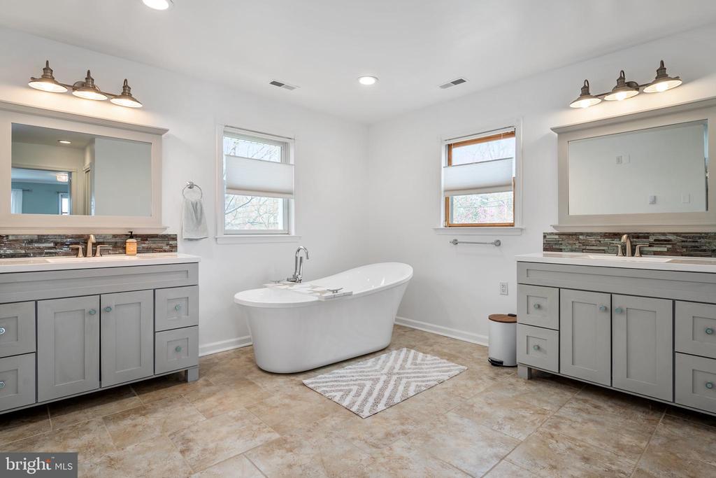Bathroom with a freestanding soaking tub between matching gray vanities and large mirrors.