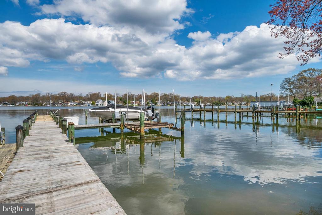 Wooden docks and sailboats line a calm marina beneath a cloud-filled blue sky.