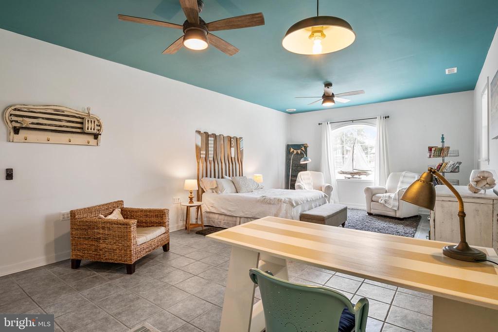 Bedroom with a teal ceiling, a bed, a foreground desk, and a sitting area by the window.