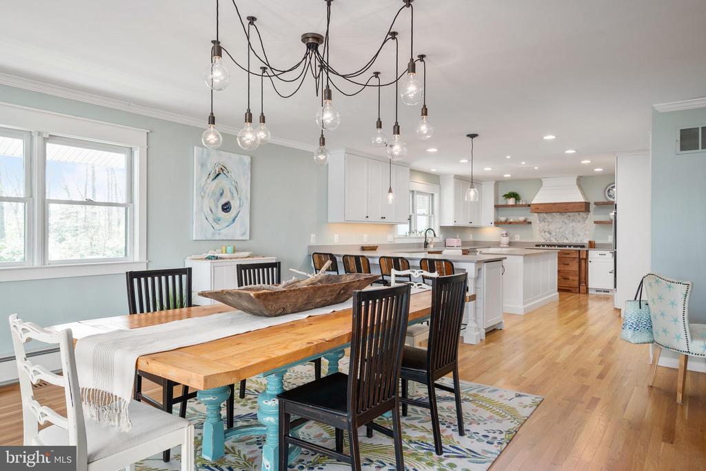 Open dining room with a long wood table, pale blue walls, and an adjoining white kitchen.