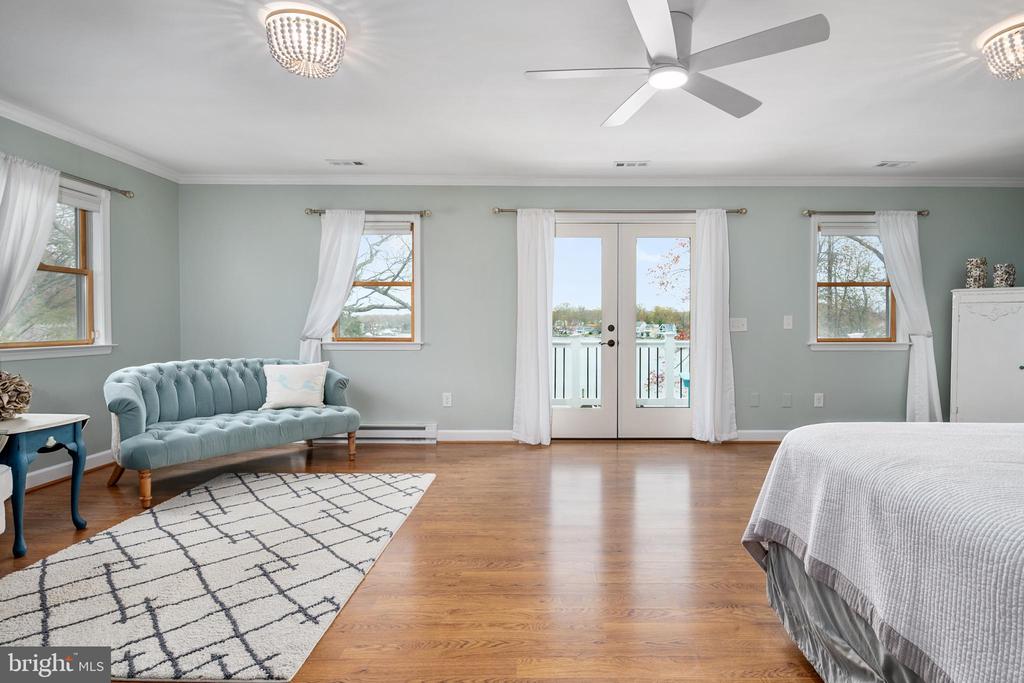 Bedroom with a blue tufted loveseat and French doors opening to a balcony overlooking the water.