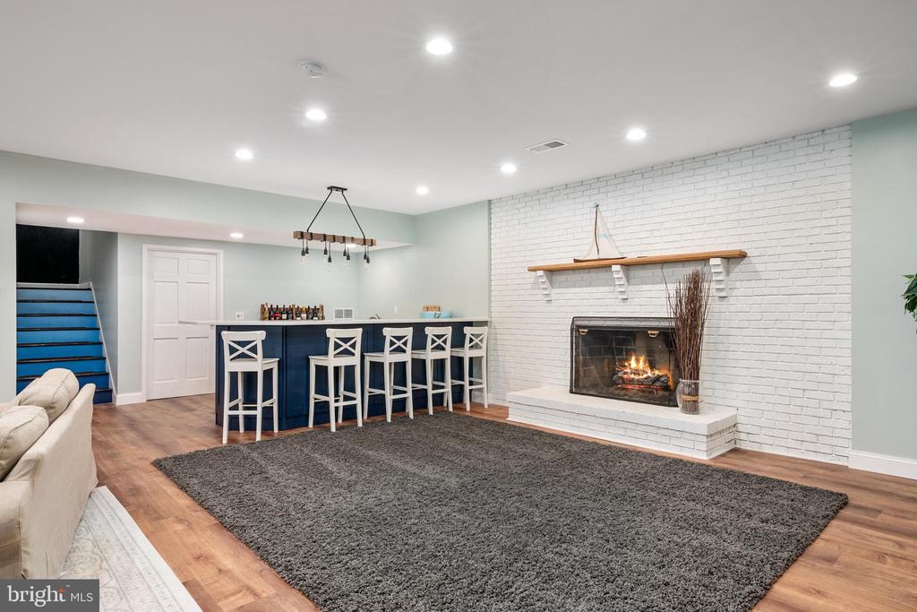 Finished basement with a navy bar, white stools, and a fireplace in a white brick wall.