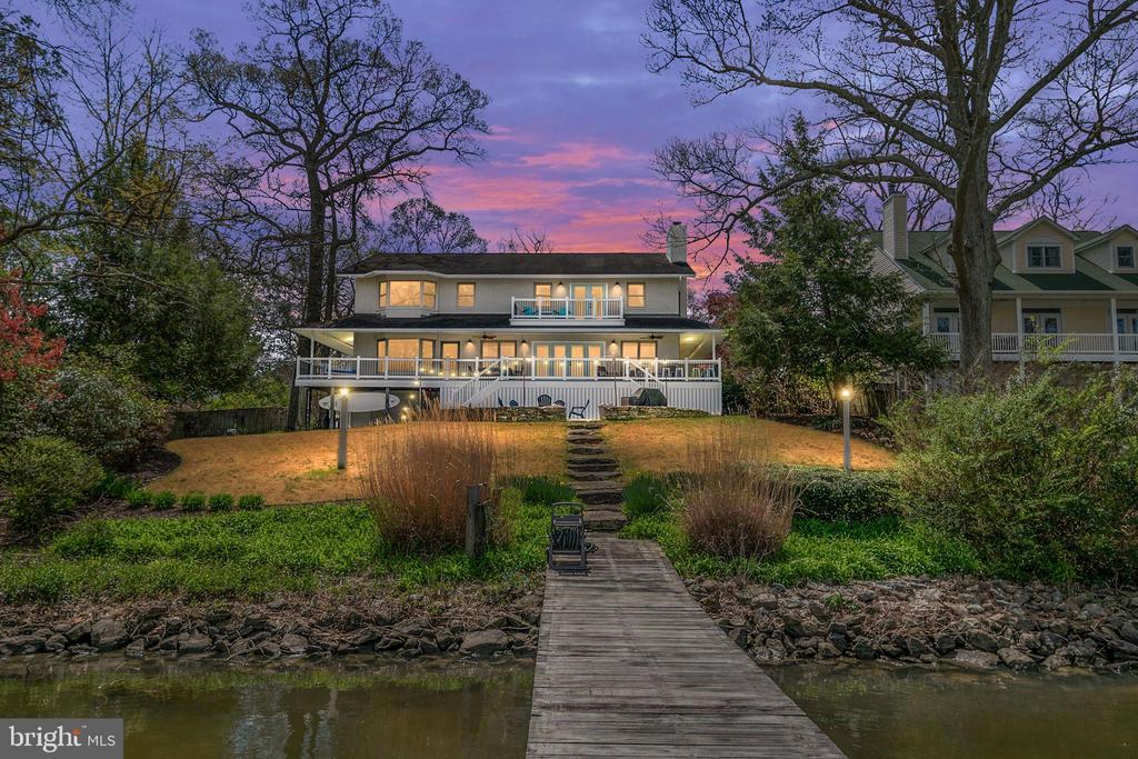 Waterfront home with a broad white deck and wooden dock at dusk.