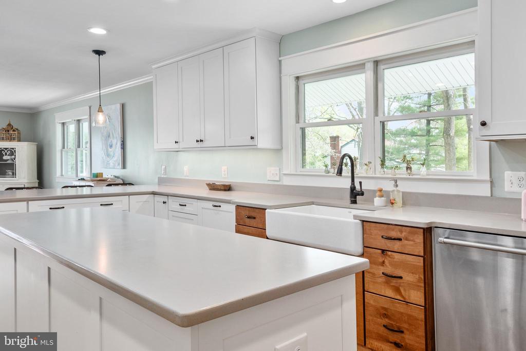 Bright kitchen with a large white island, farmhouse sink, and windows overlooking trees.