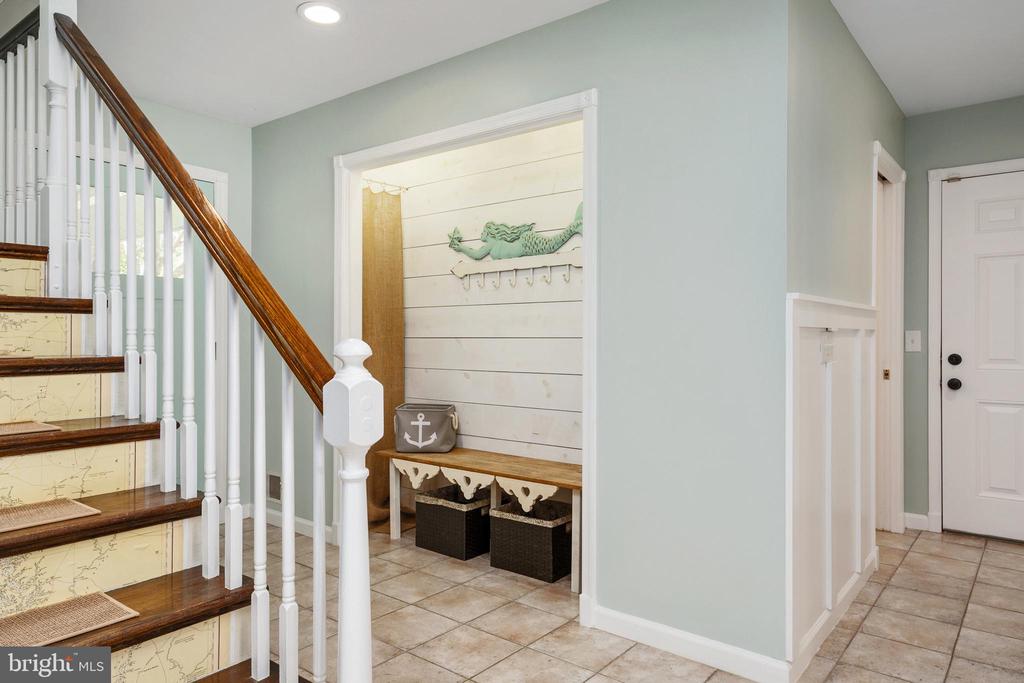 Foyer with a dark wood staircase and a bench in a shiplap entry nook.