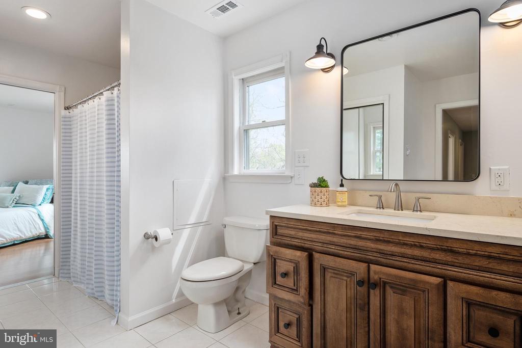 Bathroom with a wood vanity, large black-framed mirror, and striped shower curtain beside a bedroom.
