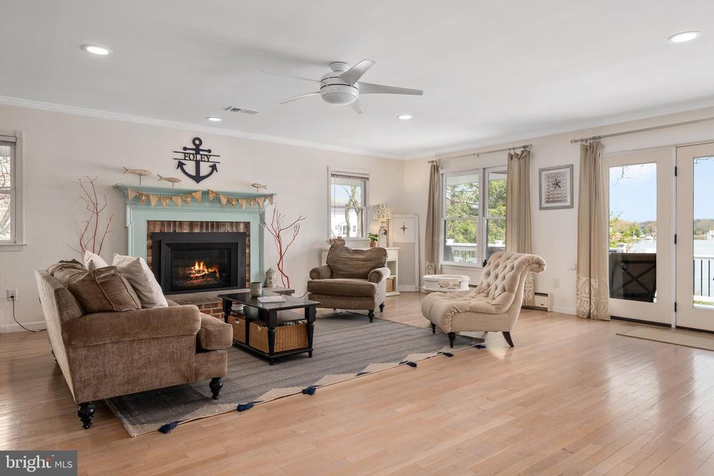 Living room with a fireplace, neutral seating, hardwood floors, and water visible through glass doors.