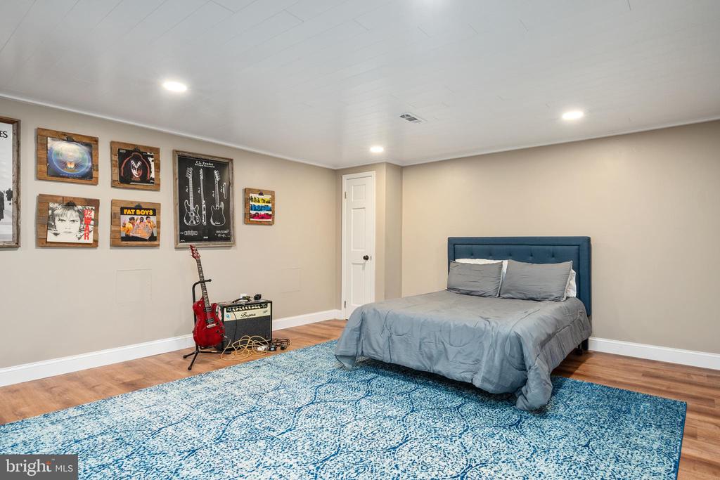 Bedroom with a blue bed and patterned rug, framed music posters, and a red electric guitar.